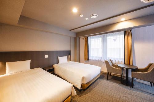 a hotel room with two beds and a table and a window at KOKO HOTEL Shimbashi Onarimon - formerly Hotel Wing International Shimbashi Onarimon in Tokyo