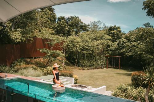 a woman in a hat standing next to a swimming pool at Te Mata Glamping in Nong Nam Daeng
