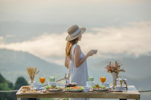 a woman in a hat holding a cup at a table with food at รีสอร์ท มอร์เม้าเท่น ดอยช้าง in Ban Thao Kaen Chan