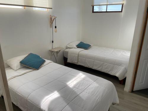 two beds in a room with white sheets and blue pillows at Hostal CKAIR in Bahia Inglesa