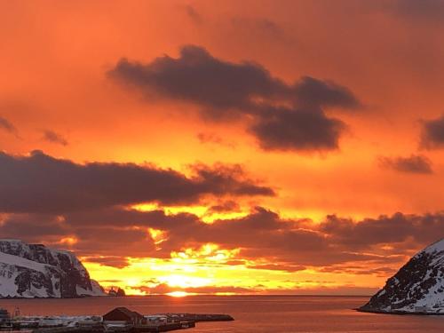 a sunset over the ocean with snow covered mountains at Overnatting Kjøllefjord, Hybelleilighet med kjøkkenkrok og eget bad in Kjøllefjord