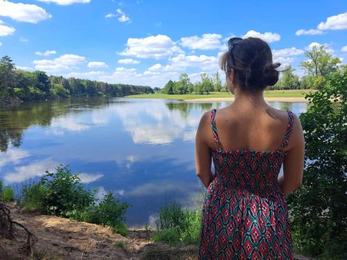 a woman is standing in front of a lake at Oaza Święty Spokój - domek z balią i jacuzzi in Rząśnik