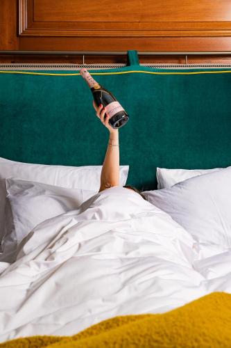 a person laying in bed with a bottle in their hand at Kimpton Clocktower by IHG in Manchester
