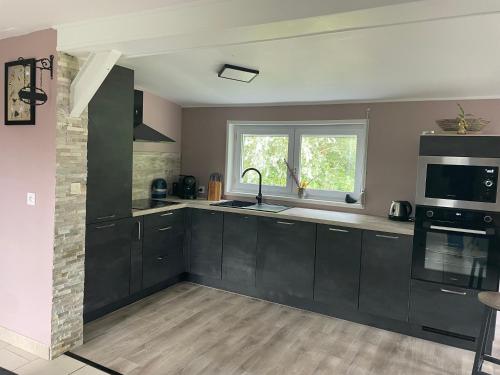 d'une cuisine avec des placards noirs, un évier et une fenêtre. dans l'établissement La maison du Marais, à Tilques