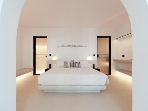 a white bedroom with a white bed and two mirrors at IKIES Santorini in Oia