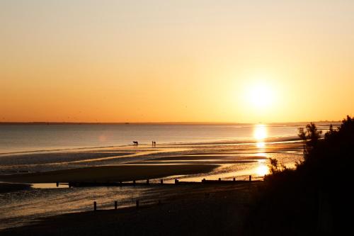 a sunset on a beach with people walking on the sand at Beachfront House w Pool & Steam in West Wittering