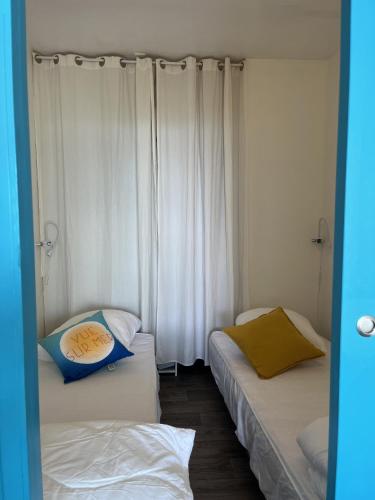 - 2 lits dans une chambre avec des rideaux blancs dans l'établissement L Arc en Ciel, à Saint-Jean-de-Monts