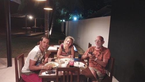 two men and a woman sitting at a table at night at Hotel white house mahiyanganaya in Mahiyangana
