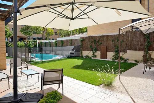a patio with an umbrella and a yard with a pool at Charming Home with Pool and Garden, Just Outside Madrid in Villanueva de la Cañada