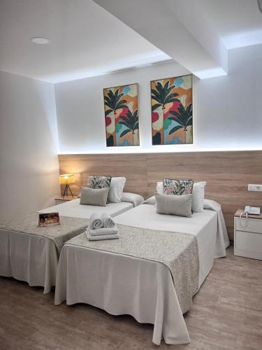 two beds in a room with paintings on the wall at Hotel Romerito in Málaga