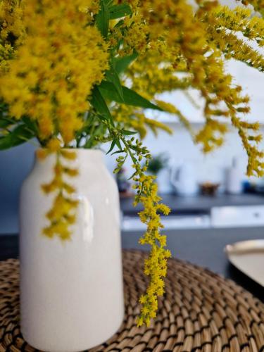 a white vase filled with yellow flowers on a table at Atpūtas Comfort Cabin House in Kalngale