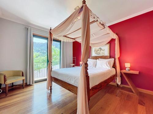 a bedroom with a canopy bed with a red wall at Casa da Palmeira in Machico