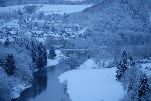 a snow covered river with a town and a bridge at La Maison Hôte, gîte de charme en bord de Semois in Bouillon