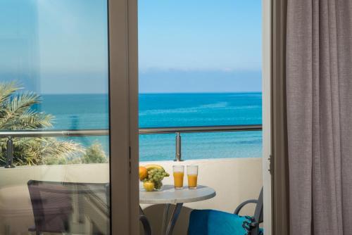 a table with two glasses of orange juice and a view of the ocean at Malliotakis Beach Hotel "by Checkin" in Stalida