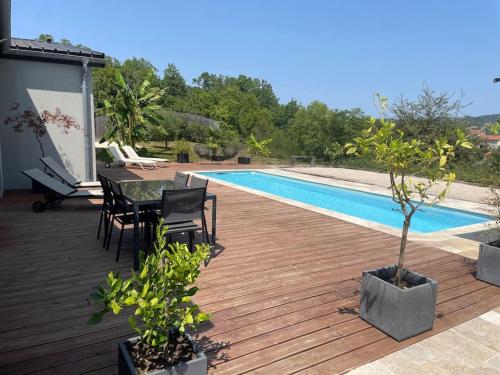 - une terrasse en bois avec une table et des chaises à côté de la piscine dans l'établissement Villa Kevin piscine, pool house et pétanque 6 à 8 personnes, à Villefranche-de-Rouergue