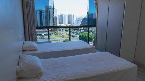 two beds in a room with a large window at Temporada - Vista Espetacular - Garvey in Brasilia