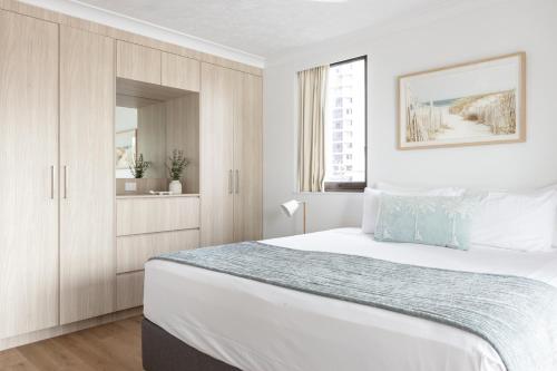 a white bedroom with a large bed and a window at Columbia Beachfront Apartments on Rainbow Bay in Gold Coast