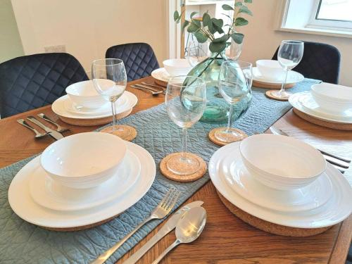 a wooden table with white plates and wine glasses at Modern Newly Refurbished 3-Bedroom House in Lincoln