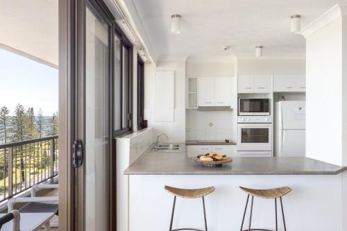 a kitchen with white cabinets and a counter with two stools at Columbia Beachfront Apartments on Rainbow Bay in Gold Coast