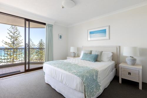a white bedroom with a bed and a balcony at Columbia Beachfront Apartments on Rainbow Bay in Gold Coast