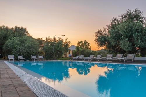 a swimming pool with chairs and a sunset in the background at Armandiola in Cardedu