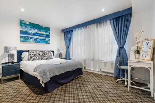 een slaapkamer met blauwe gordijnen, een bed en een bureau bij Westminster Classic Massionette in Londen