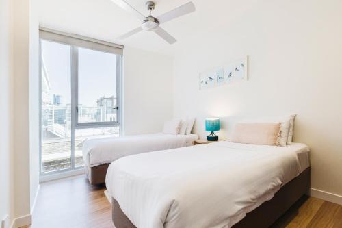 two beds in a room with a large window at Easy Eastside - Urban Chic with a Rooftop Pool Oasis in Melbourne