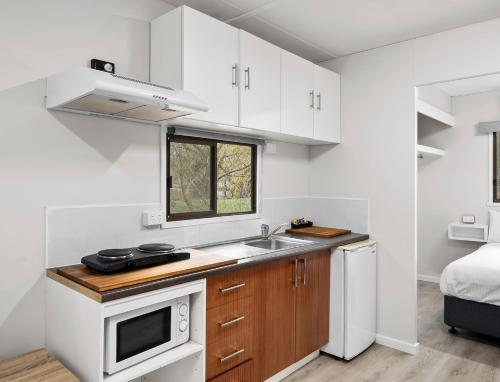 a kitchen with white cabinets and a sink and a bed at Shepparton Holiday Park and Village in Shepparton