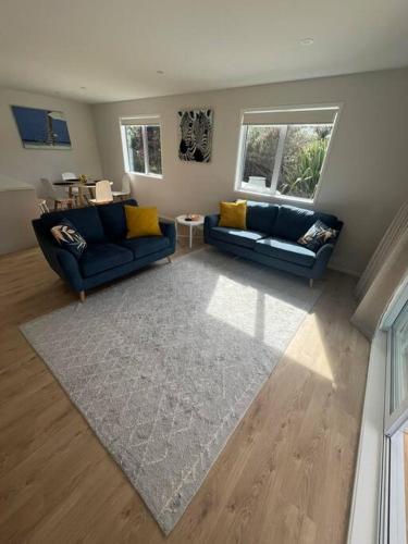 a living room with two blue couches and a rug at Bach At 45 in Ahipara