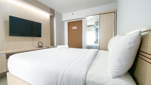 a bedroom with a white bed and a television at Cozy Living and Homey Studio Room Cinere Resort Apartment By Travelio in Depok