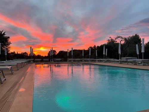 a large swimming pool with a sunset in the background at Hotel Castel Miramonti in Selva di Fasano