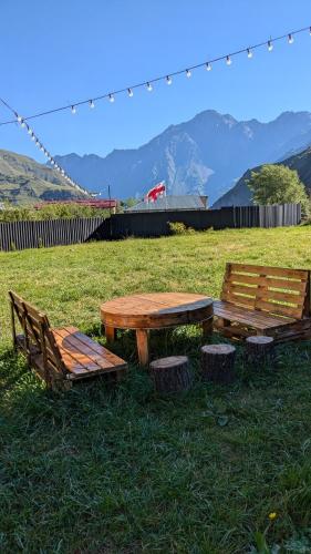 two wooden benches and a picnic table in a field at Rest point cottage Kazbegi in Stepantsminda