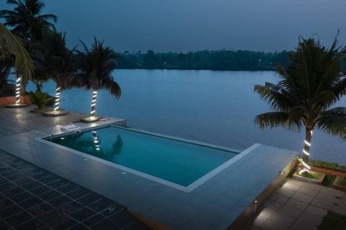 a swimming pool next to a body of water at Riveria Portico - River side 6 bedroom private pool Bungalow in Parūr