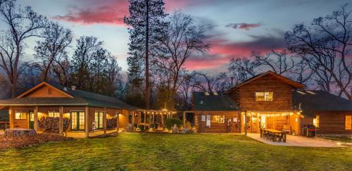 Una casa de troncos con un patio iluminado al anochecer en Log Cabin sleeps 20 with hot tub, EV Charger, firepit, en Ahwahnee