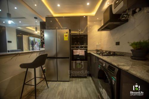 a kitchen with a stainless steel refrigerator and a stool at Blessedlife Apartment in Kumasi