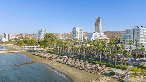 a beach with chairs and palm trees and buildings at The GrandResort - Limited Edition by Leonardo Hotels in Limassol