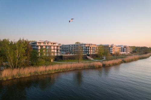einem Fluss mit Gebäuden im Hintergrund und einem Vogel, der über der Erde fliegt in der Unterkunft Brand-New Apartment EYE ON BALTIC SEA Luxurious Spa Escape in Dziwnów with Stunning Views in Dziwnów