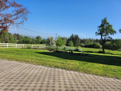 a field of grass with a white fence and a sidewalk at Gîte cozy en pleine forêt in Bining-lès-Rohrbach