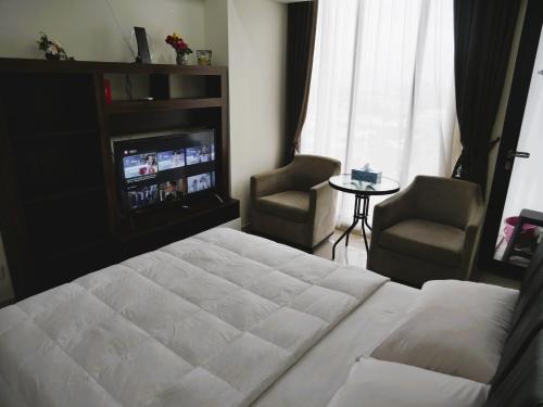 a bedroom with a bed and two chairs and a television at Meisterstadt Pollux Habibie in Batam Center