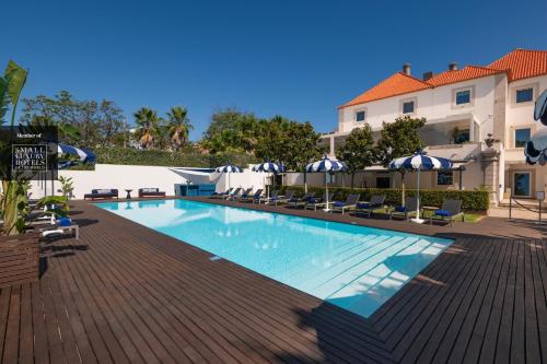 a swimming pool with chairs and umbrellas next to a building at Palácio do Governador - Lisbon Hotel & Spa in Lisbon