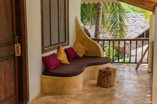 a bench with pillows on a porch with a tree stump at Mr Kahawa in Paje