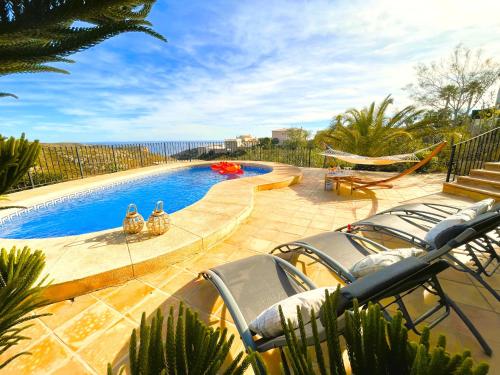 ein Pool mit Stühlen und einer Hängematte neben dem Meer in der Unterkunft Traumvilla Mimosa, Costa Blanca in Cumbre del Sol