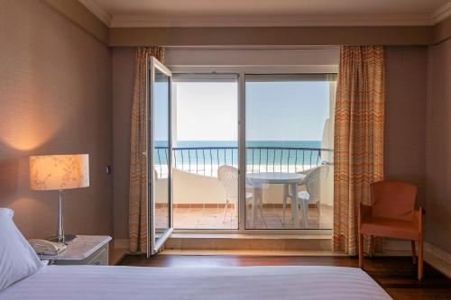 a bedroom with a bed and a balcony with a table and chairs at Hotel Playa Victoria in Cádiz
