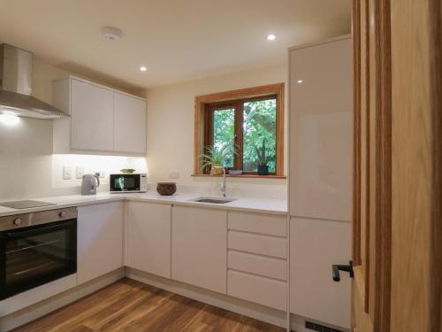 a kitchen with white cabinets and a window at Yew Tree Cottage in Dartford