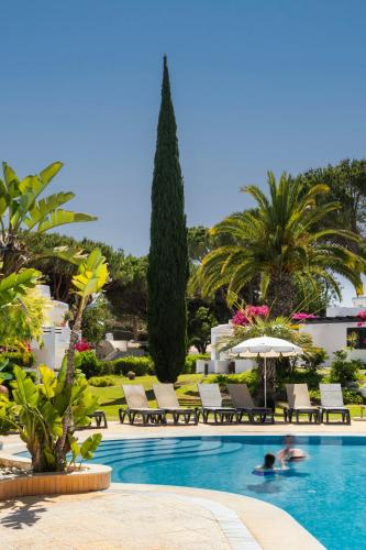 a pool with chairs and trees and a person swimming at Balaia Golf Village in Albufeira