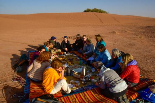 a group of people sitting around a table in the desert at Mhamid Nomad Camp in Mhamid
