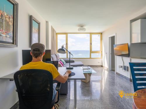 un hombre sentado en un escritorio en una habitación en Living Las Canteras Homes - Seaview, en Las Palmas de Gran Canaria