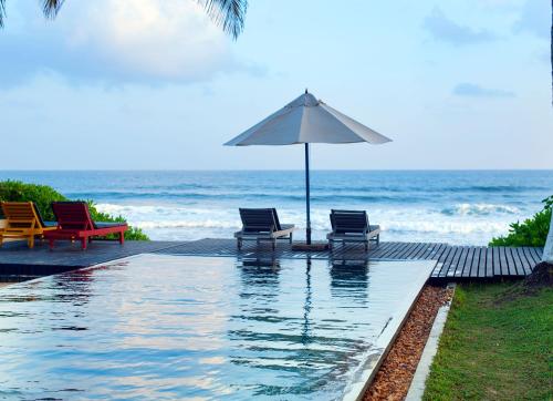 a pool with chairs and an umbrella next to the ocean at Apa Villa Thalpe in Unawatuna