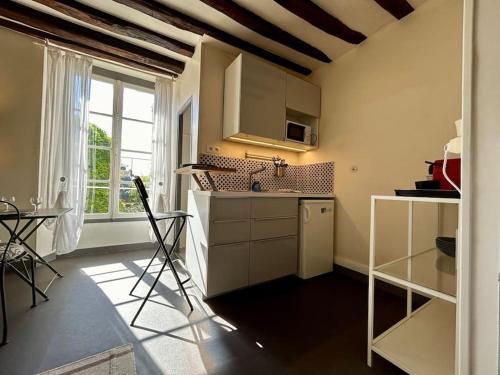une cuisine avec des armoires blanches, une table et une fenêtre dans l'établissement Studio St Merry - Fontainebleau, à Fontainebleau