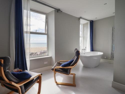a bathroom with a tub and two chairs and a large window at Tonnau Yr Oleu or Waves of Light in Barmouth